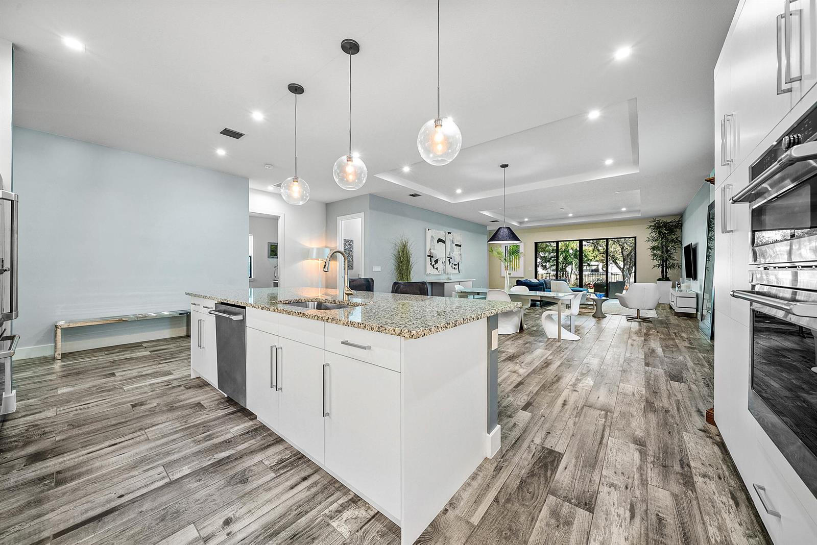A modern kitchen with white cabinetry, granite countertops, and pendant lighting overlooks an open living area — 3069 Safflower Circle, West Palm Beach FL 33401, WEST PALM BEACH, FL