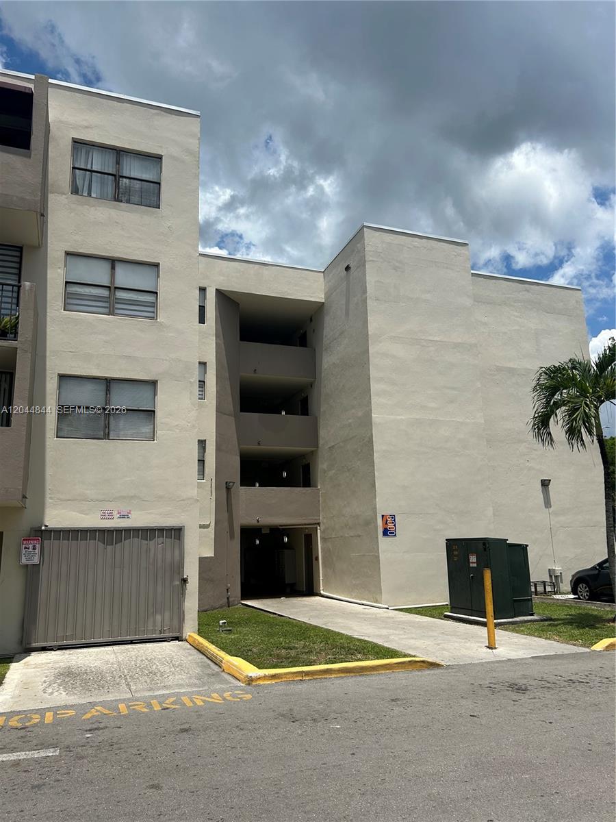 A multi-story beige apartment building features a ground-level gated entrance and a paved walkway — MIAMI, FL