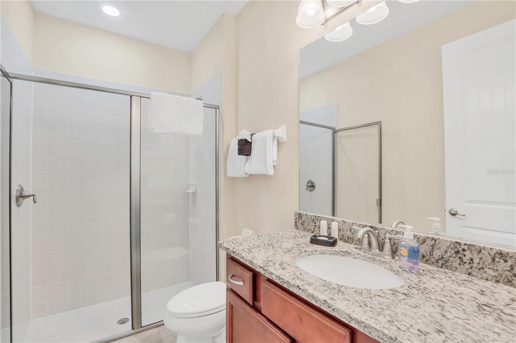 A bathroom features a granite vanity, a wooden cabinet, a toilet, and a glass-enclosed shower — 801 LASSO DRIVE, KISSIMMEE, FL