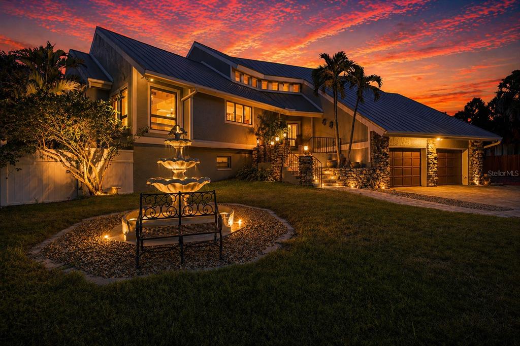 A multi-level house at dusk features a tiered fountain, a metal roof, and stone accents — 4024 CASEY KEY ROAD, NOKOMIS, FL