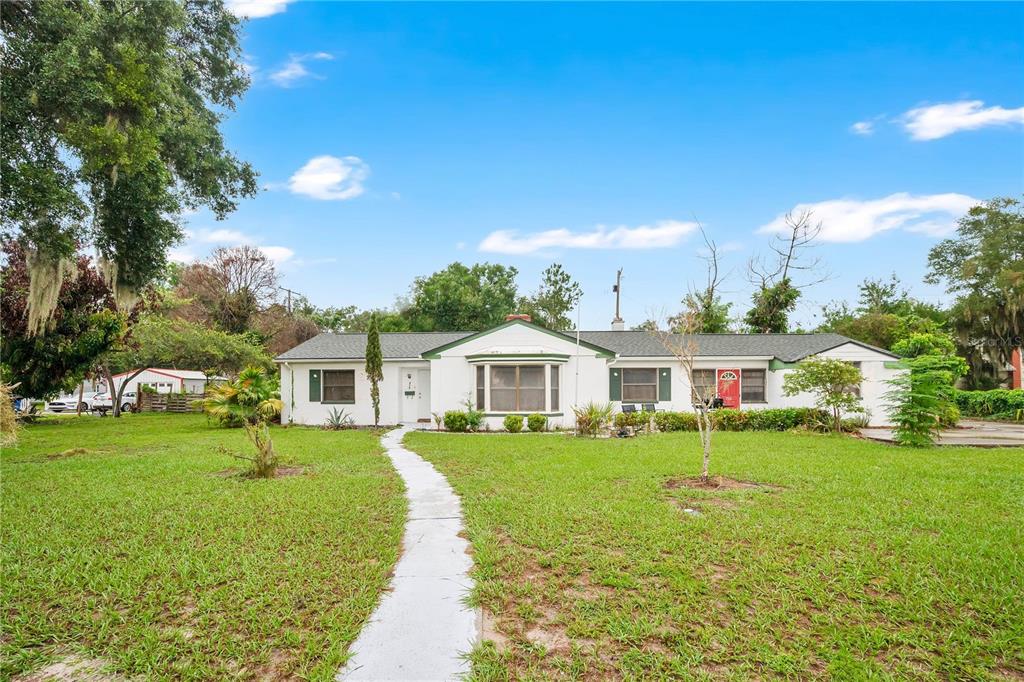 A single-story white house with a green roof sits on a large grassy lot — 715 AVENUE B SW, WINTER HAVEN, FL
