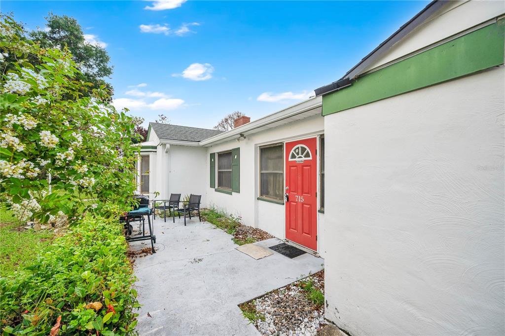 A white house exterior features a red front door, green trim, and a concrete patio — 715 AVENUE B SW, WINTER HAVEN, FL