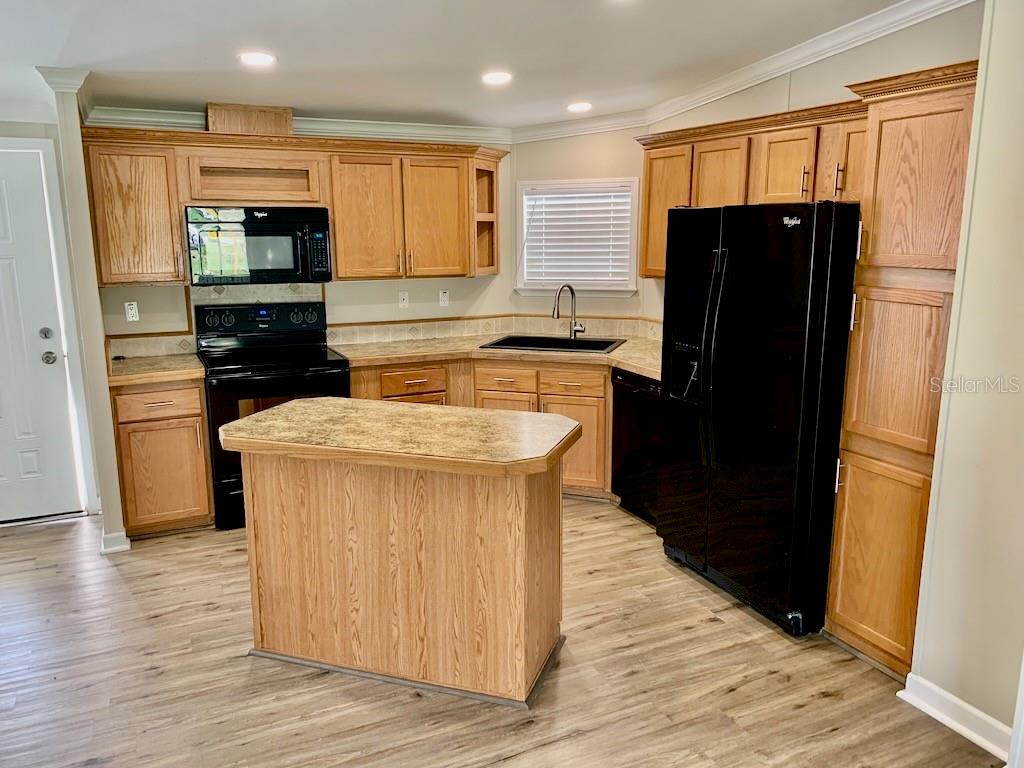 A kitchen features oak cabinets, black appliances, a central island, and light wood-look flooring — 6632 JACK STREET, PUNTA GORDA, FL