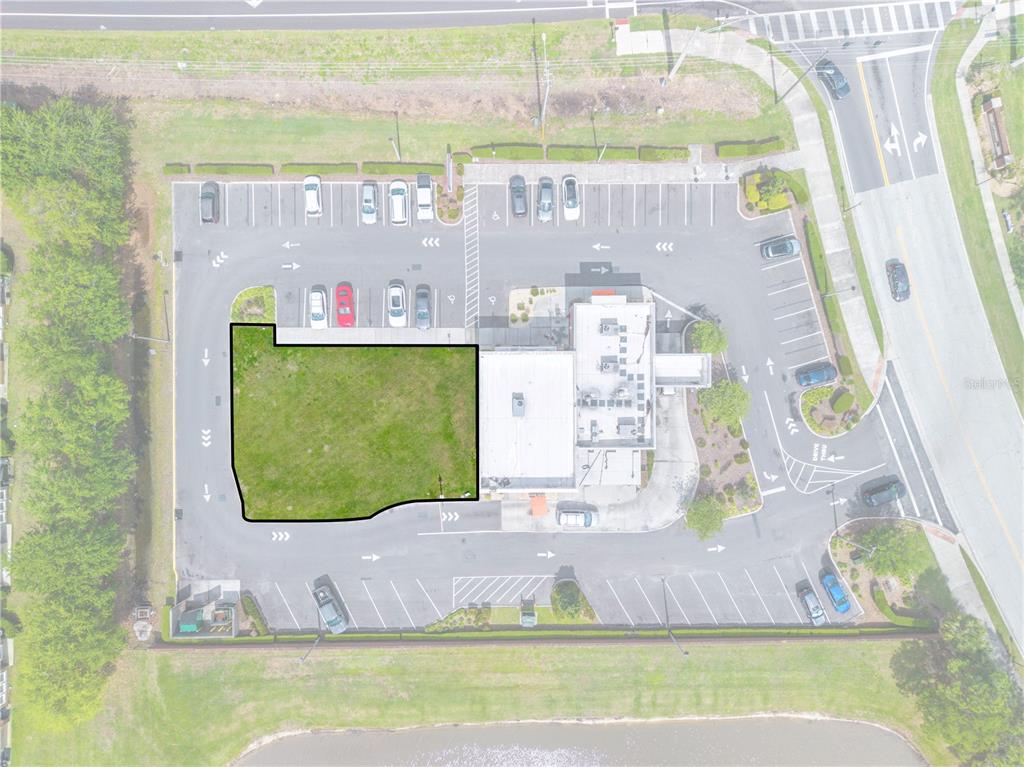 An aerial view shows a vacant, grass-covered lot outlined in black next to a commercial building — 1591 JOHN YOUNG PKWY, KISSIMMEE, FL
