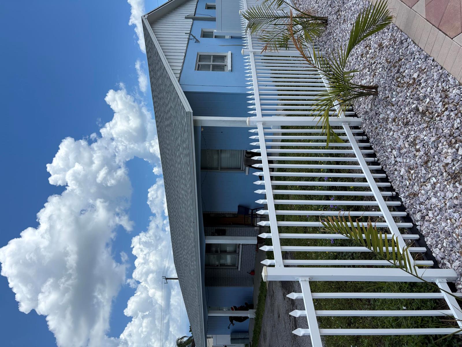 A blue house with a white picket fence and a gravel yard under a cloudy sky — 3308 Lake Avenue, West Palm Beach FL 33405, WEST PALM BEACH, FL