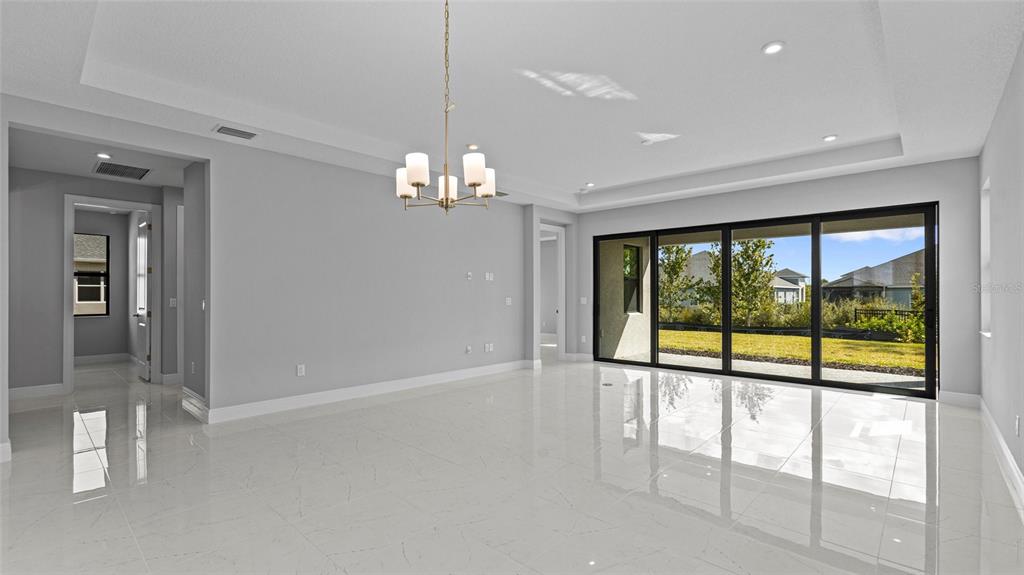 A bright, empty living room features white tiled floors, a tray ceiling, and sliding glass doors — 14363 HAMMOCK OAK STREET, PARRISH, FL