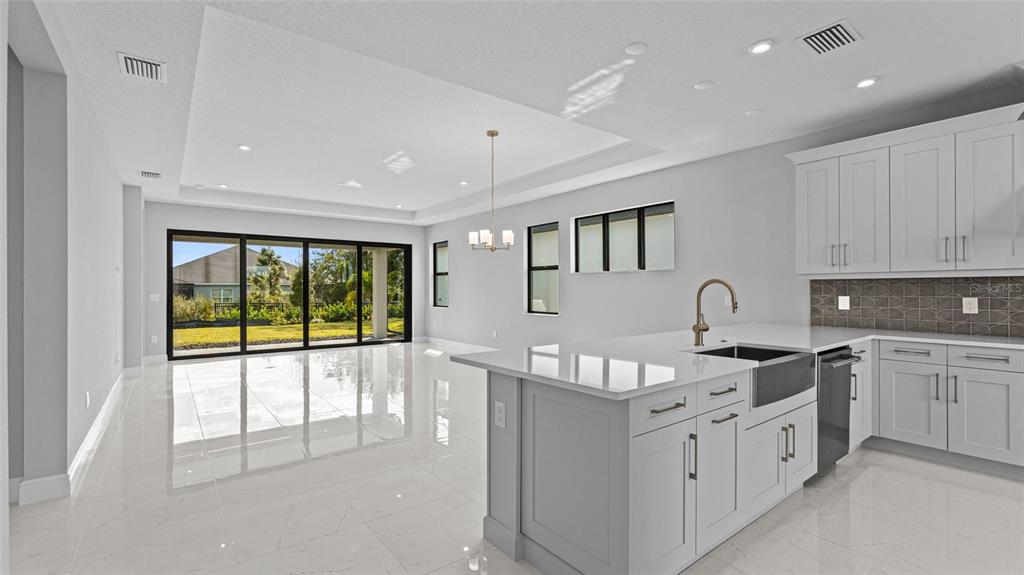 A modern kitchen with a large island and white cabinets opens to a bright living area — 14363 HAMMOCK OAK STREET, PARRISH, FL