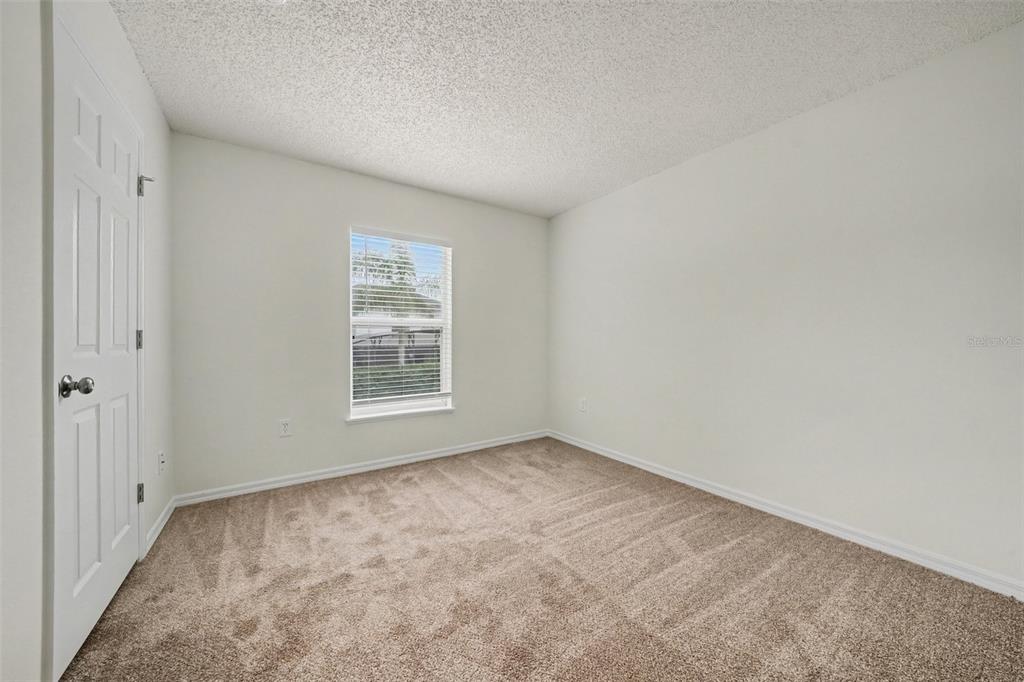 An empty bedroom features beige carpet, white walls, a textured ceiling, and a single window — 1099 WELCH HILL CIRCLE, APOPKA, FL