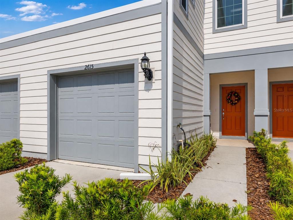 The exterior of a townhouse features a gray garage, a brown front door, and landscaping — 2615 WINSOME WAY, DAVENPORT, FL