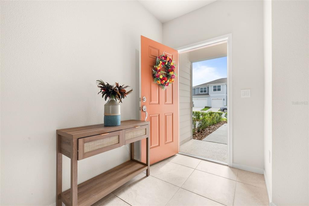 An entryway features a light wood console table, a coral front door, and tiled flooring — 2615 WINSOME WAY, DAVENPORT, FL