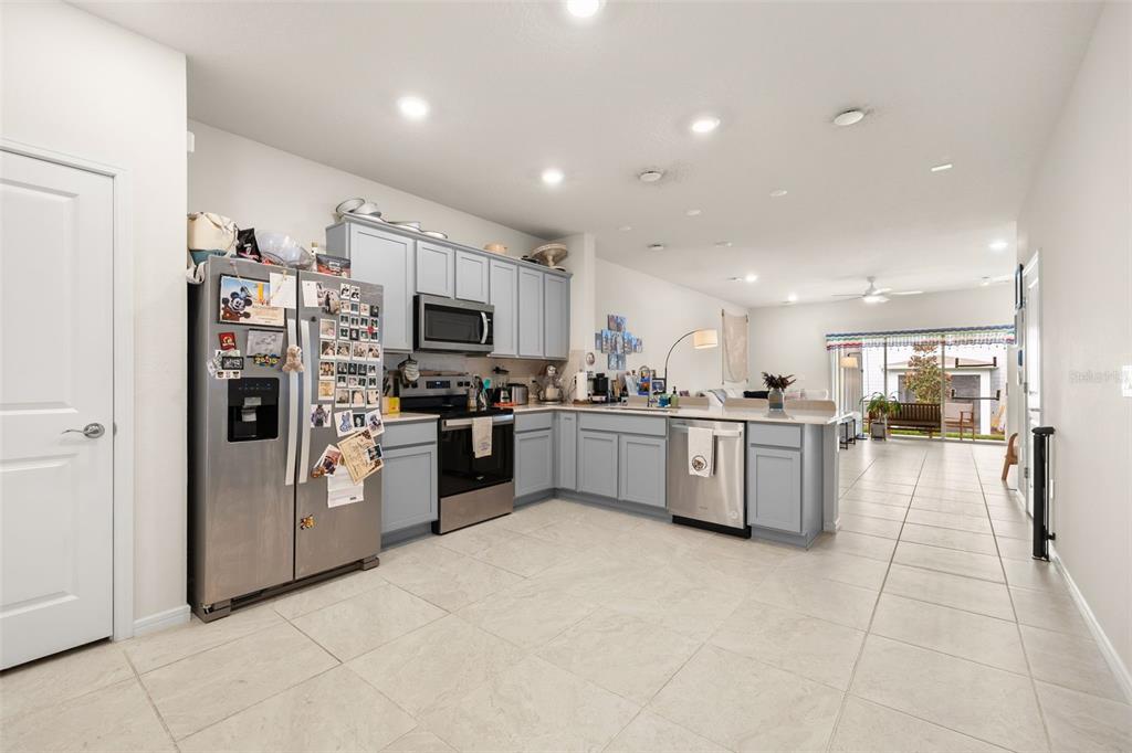 A kitchen with light blue cabinets, stainless steel appliances, and tile flooring opens to a living area — 2615 WINSOME WAY, DAVENPORT, FL