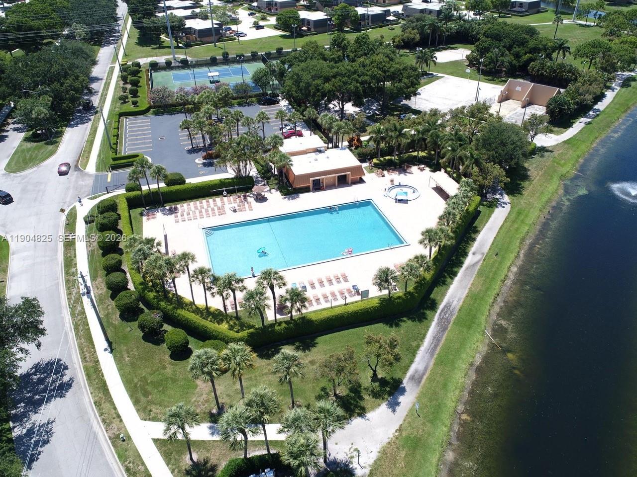 An aerial view shows a swimming pool, tennis courts, and a clubhouse next to a lake — 157 Heritage Way, West Palm Beach FL 33407, WEST PALM BEACH, FL