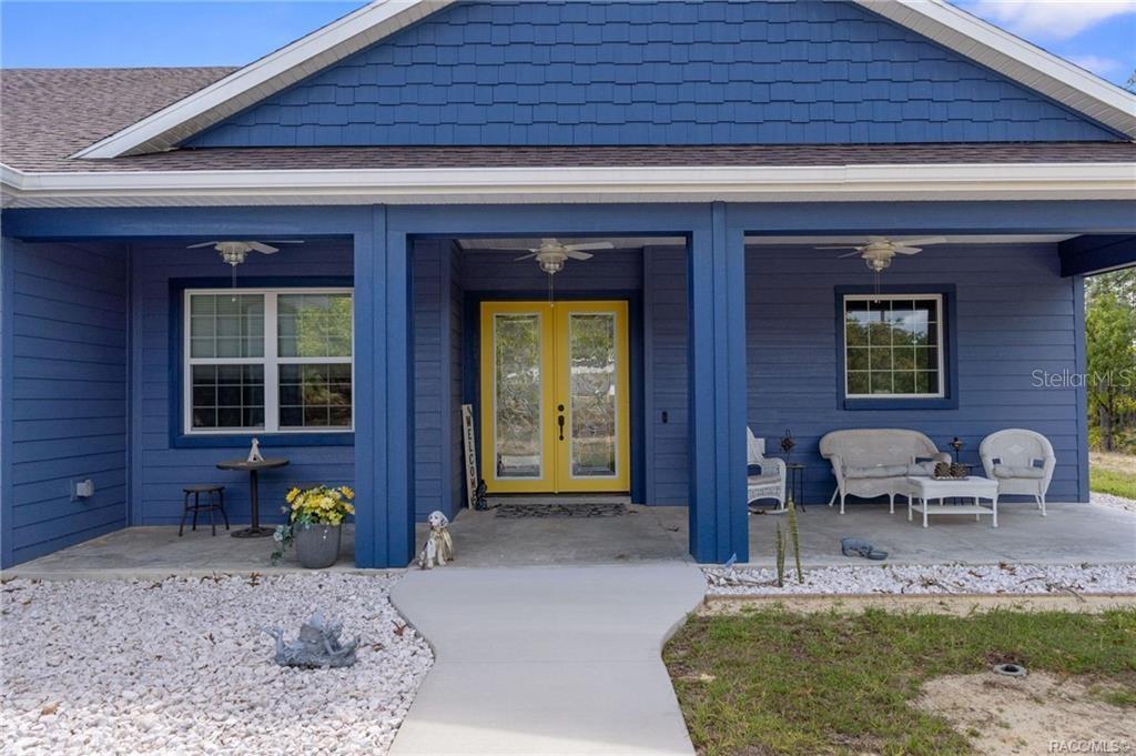 A blue house exterior features a covered porch, yellow double doors, and white gravel landscaping — 4999 N TEE PEE DRIVE, BEVERLY HILLS, FL