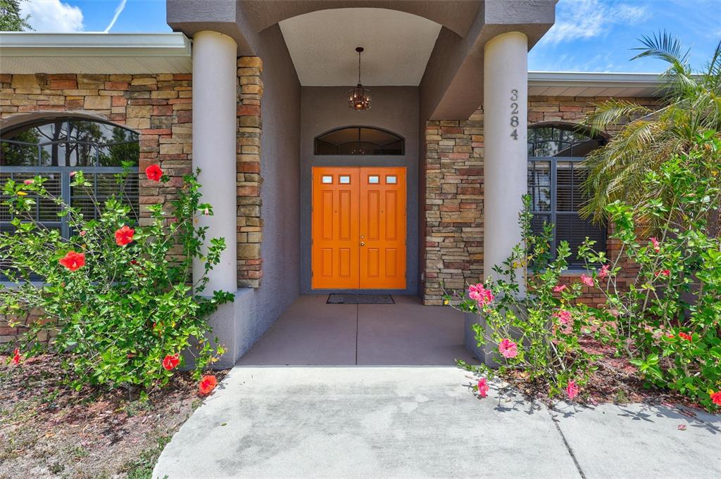The front entrance of a house features bright orange double doors and stone exterior walls — 3284 NEWMARK STREET, NORTH PORT, FL
