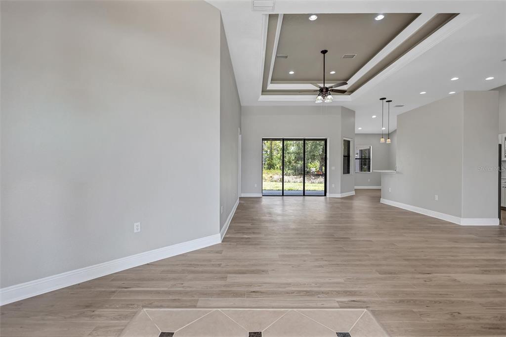 An open-concept living area features light wood-look flooring, a tray ceiling, and sliding glass doors — 3284 NEWMARK STREET, NORTH PORT, FL