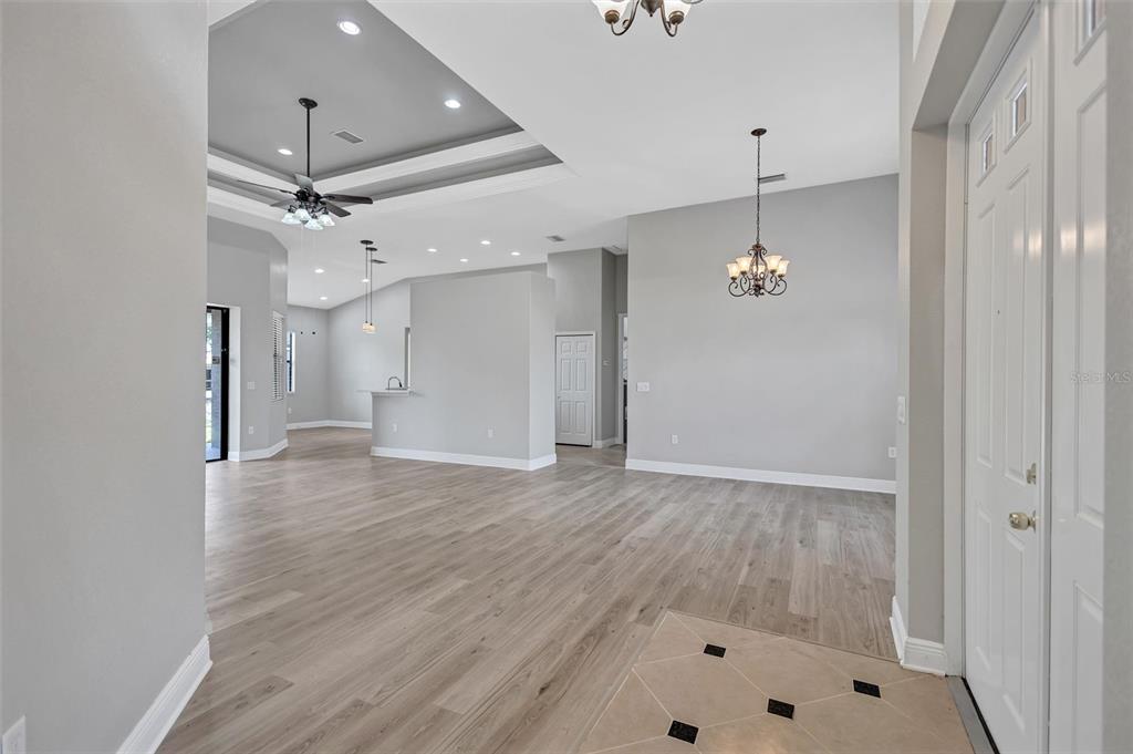 An open-concept living area features light wood-look flooring, a tray ceiling, and a chandelier — 3284 NEWMARK STREET, NORTH PORT, FL