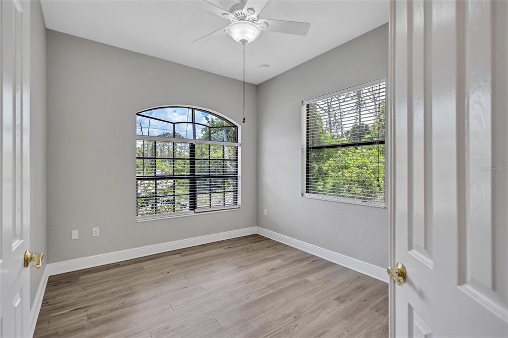 An empty room with light gray walls, wood-look flooring, a ceiling fan, and two windows — 3284 NEWMARK STREET, NORTH PORT, FL