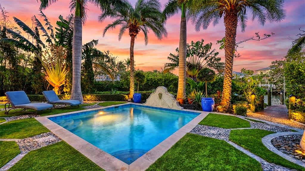 A rectangular swimming pool sits in a landscaped backyard with palm trees at sunset — 513 VILLA ROSA WAY, ANNA MARIA, FL