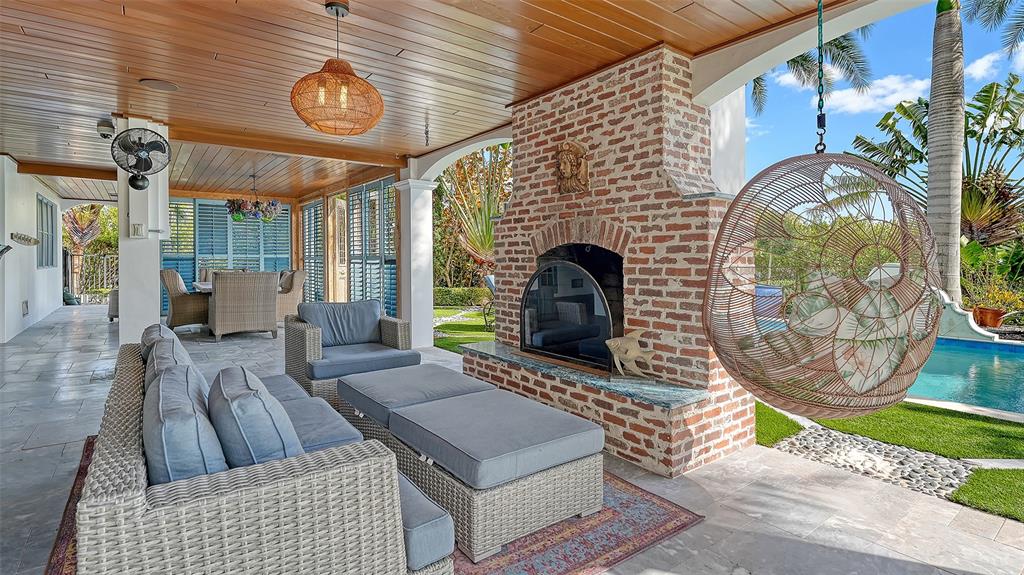 A covered outdoor patio features a brick fireplace, wicker furniture, and a hanging chair — 513 VILLA ROSA WAY, ANNA MARIA, FL