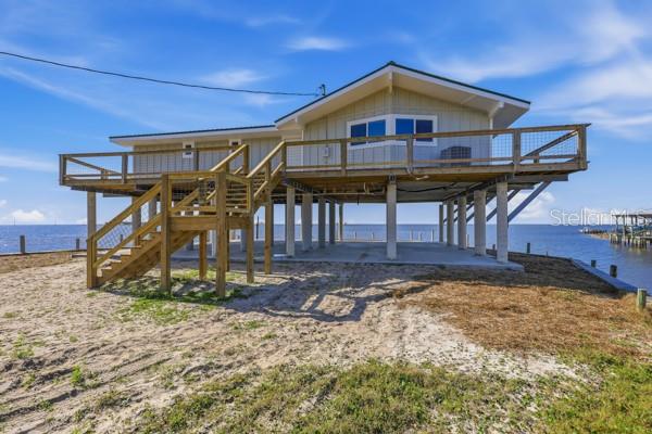 A stilt house with a wooden deck and staircase stands on a sandy waterfront lot — 18 4TH STREET, HORSESHOE BEACH, FL