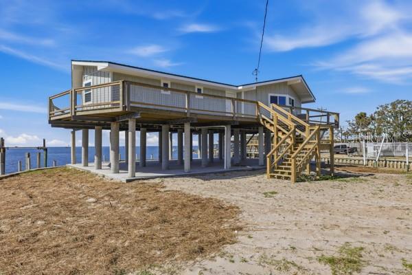 A stilt house with a wooden deck and staircase stands on a sandy waterfront lot — 18 4TH STREET, HORSESHOE BEACH, FL