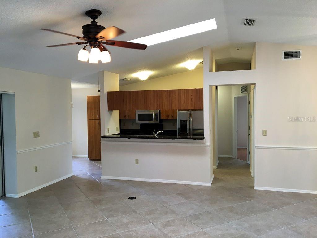 A kitchen with wood cabinets and a breakfast bar overlooks a tiled living area — 2278 CORK OAK STREET W, SARASOTA, FL
