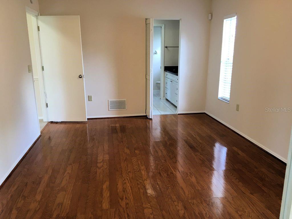 An empty room with hardwood floors, a white door, and an open doorway to a bathroom — 2278 CORK OAK STREET W, SARASOTA, FL