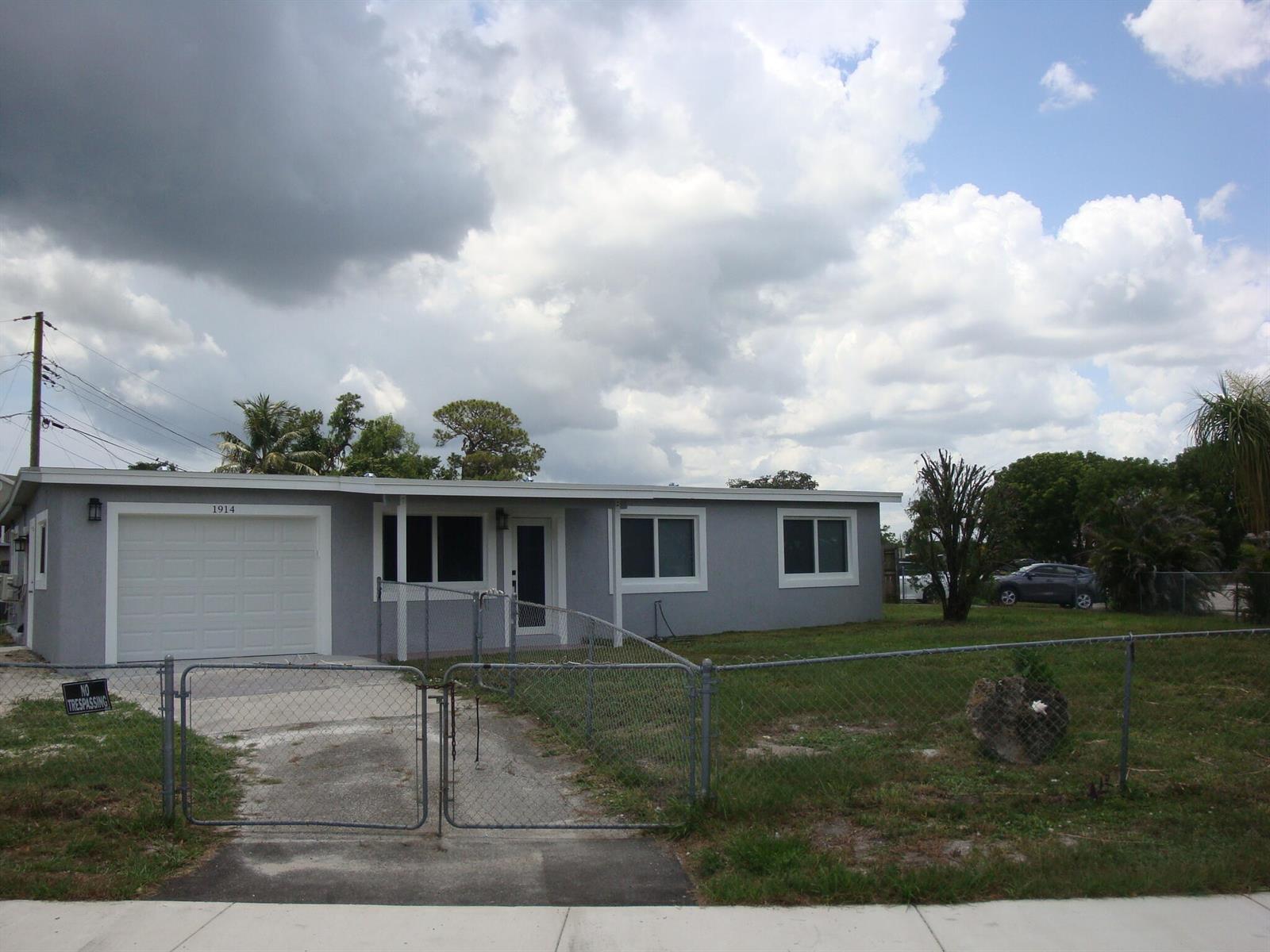 A single-story gray house with a white garage door and a chain-link fence — 1914 Kudza Road, West Palm Beach FL 33415, WEST PALM BEACH, FL