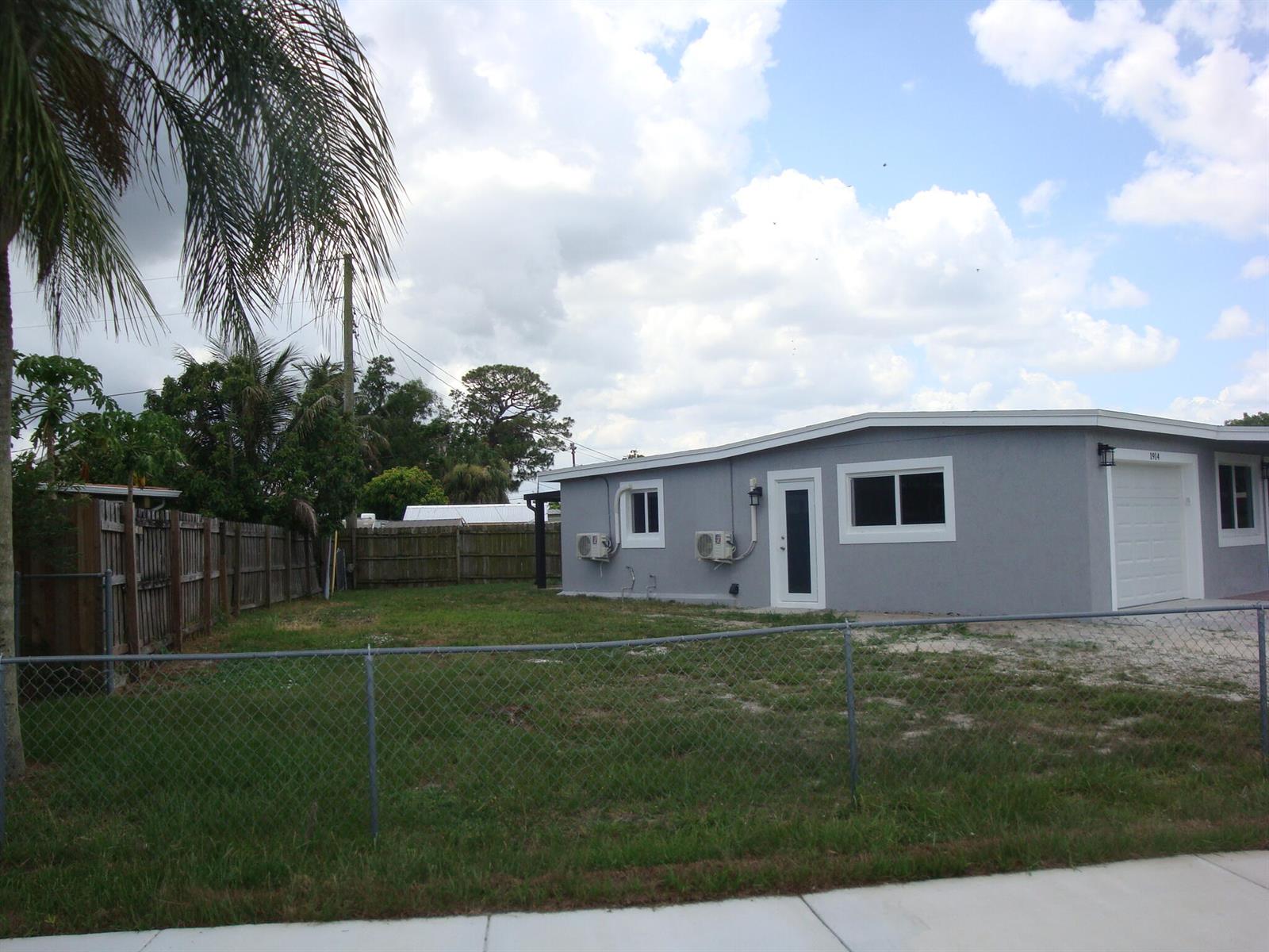 A gray single-story house with a white garage door and a chain-link fence — 1914 Kudza Road, West Palm Beach FL 33415, WEST PALM BEACH, FL