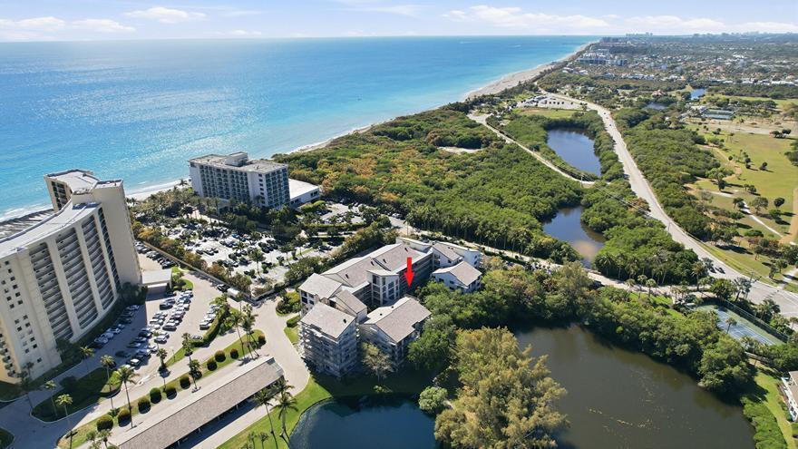 An aerial view shows a multi-story residential complex near a beach, ponds, and vegetation — 500 Ocean Trail Way # 207, Jupiter FL 33477, JUPITER, FL