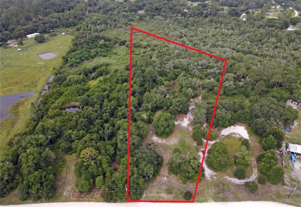 An aerial view shows a wooded, trapezoidal plot of land outlined in red near a road — 432 WILDLIFE TRAIL, LAKELAND, FL
