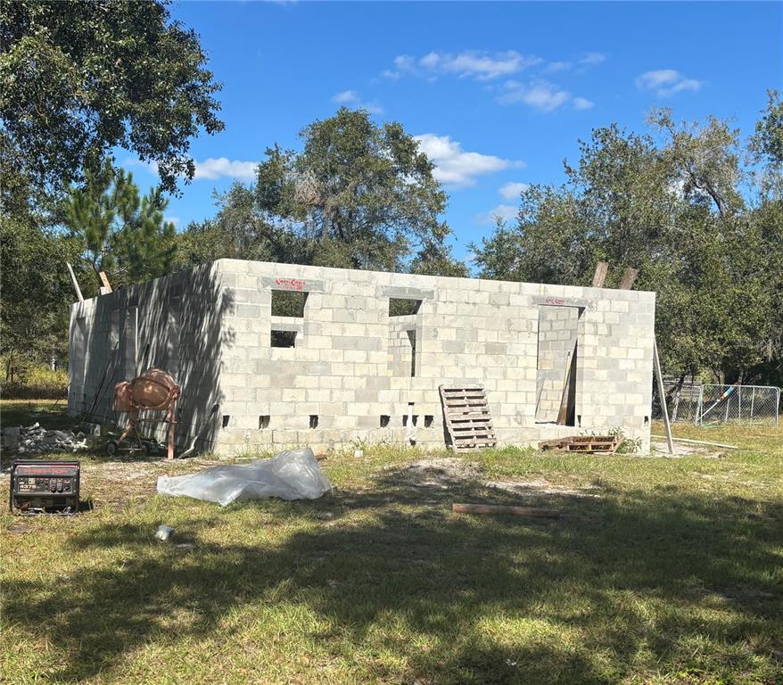 An unfinished concrete block structure stands in a grassy, wooded lot under a blue sky — 432 WILDLIFE TRAIL, LAKELAND, FL