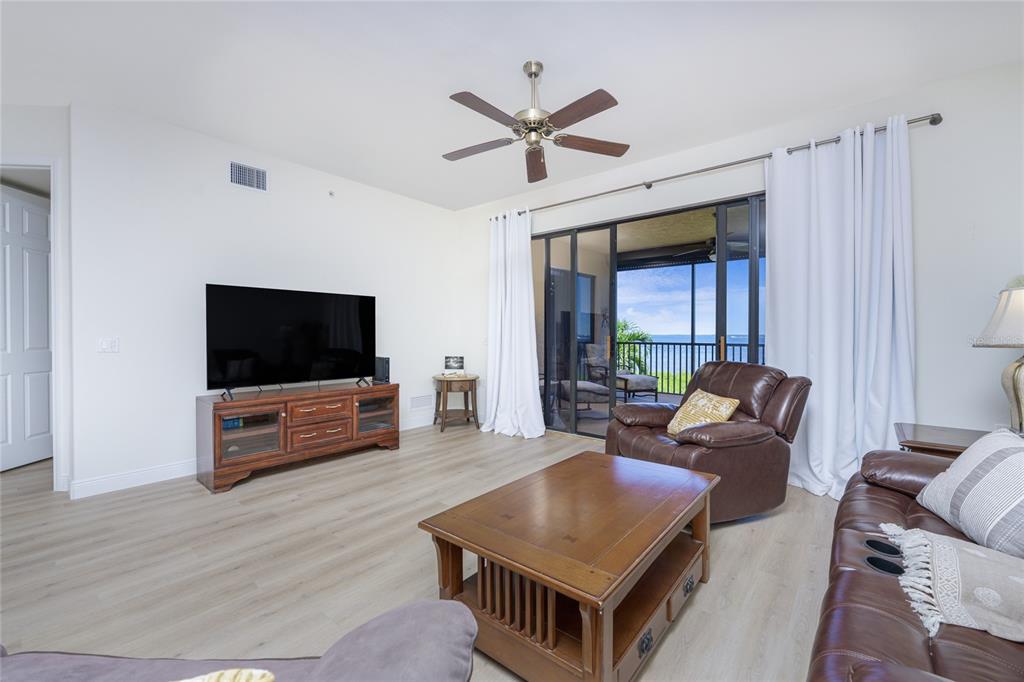 A living room features wood-look flooring, a ceiling fan, a television console, and a balcony view — 85 VIVANTE BOULEVARD UNIT 8524, PUNTA GORDA, FL