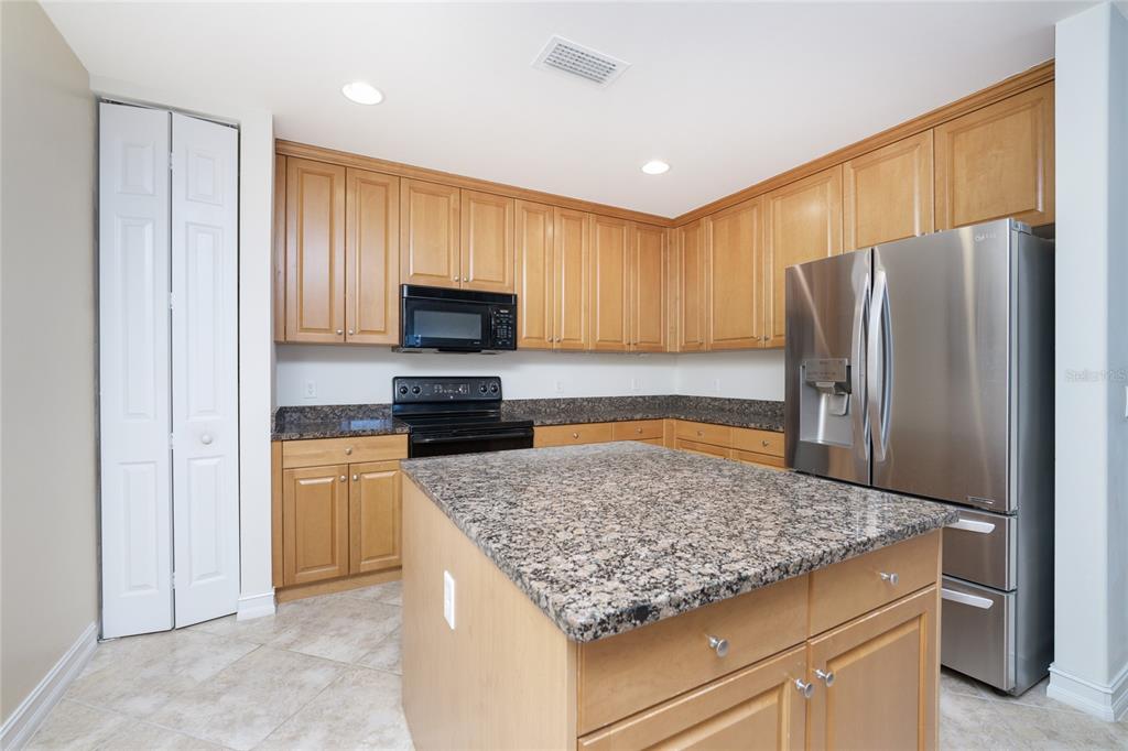 A kitchen features light wood cabinets, granite countertops, a center island, and stainless steel appliances — 85 VIVANTE BOULEVARD UNIT 8524, PUNTA GORDA, FL