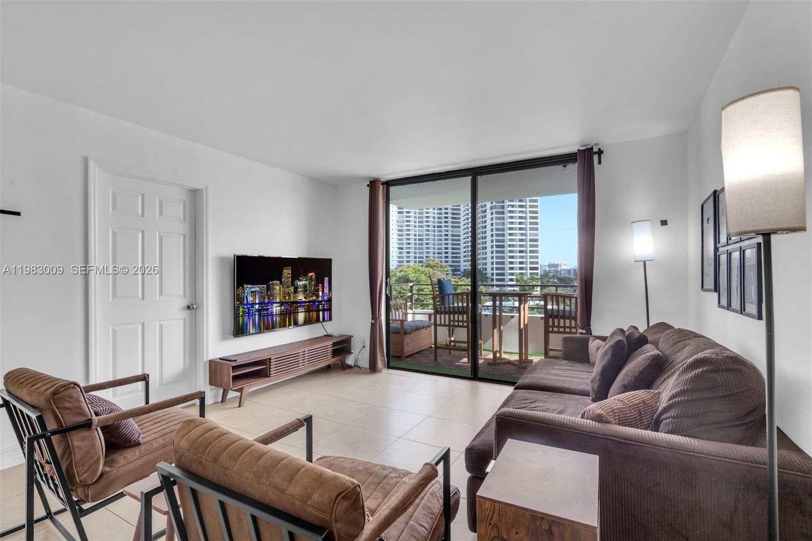 A living room features a brown sofa, two armchairs, a television, and a balcony view — 500 Three Islands Blvd # 226, Hallandale Beach FL 33009, HALLANDALE BEACH, FL