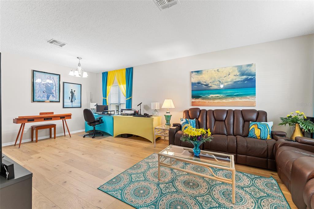 A living room features light wood floors, a brown leather sofa, and a dual-colored desk — 3605 CAPE COURT, ST CLOUD, FL