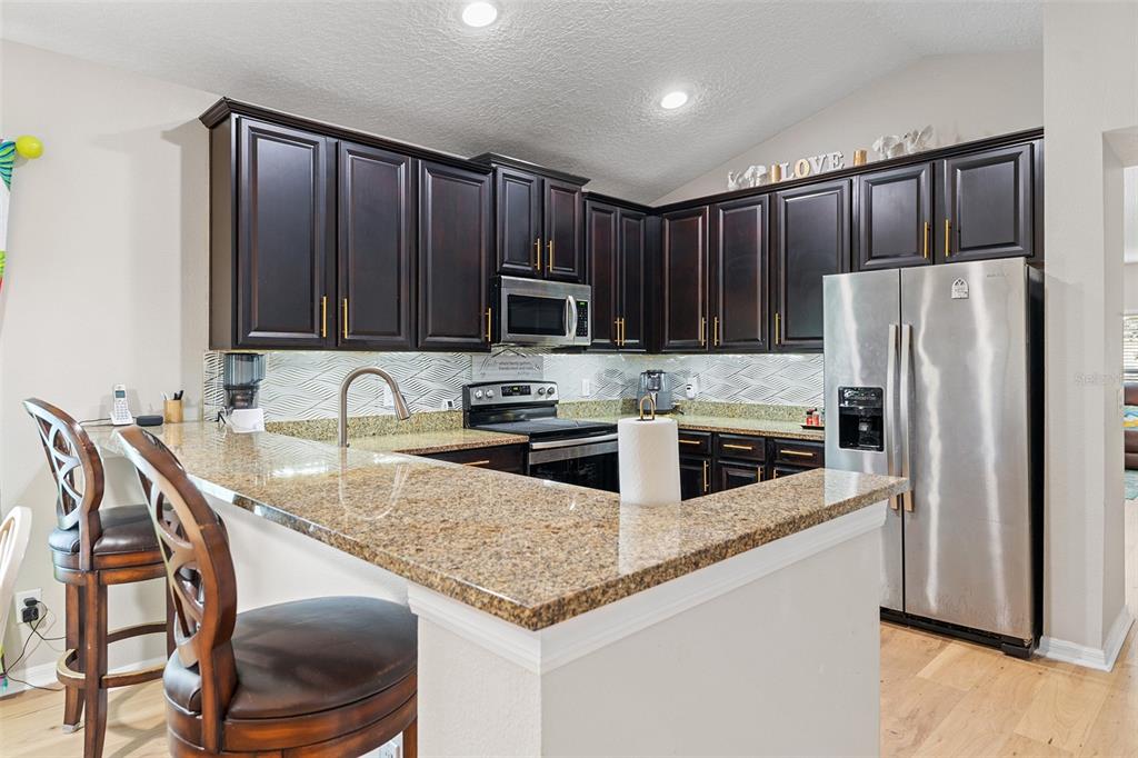 A kitchen features dark wood cabinets, granite countertops, stainless steel appliances, and a breakfast bar — 3605 CAPE COURT, ST CLOUD, FL