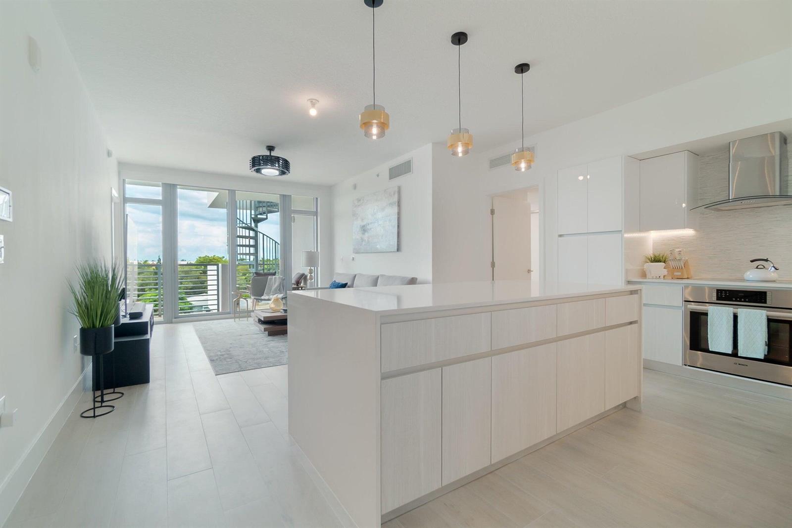 A modern kitchen with a white island overlooks a living area with a spiral staircase — 111 SE 1st Avenue # 514, Delray Beach FL 33444, DELRAY BEACH, FL