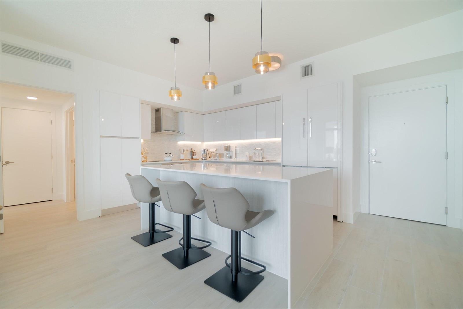 A modern white kitchen features a central island with three grey bar stools and pendants — 111 SE 1st Avenue # 514, Delray Beach FL 33444, DELRAY BEACH, FL