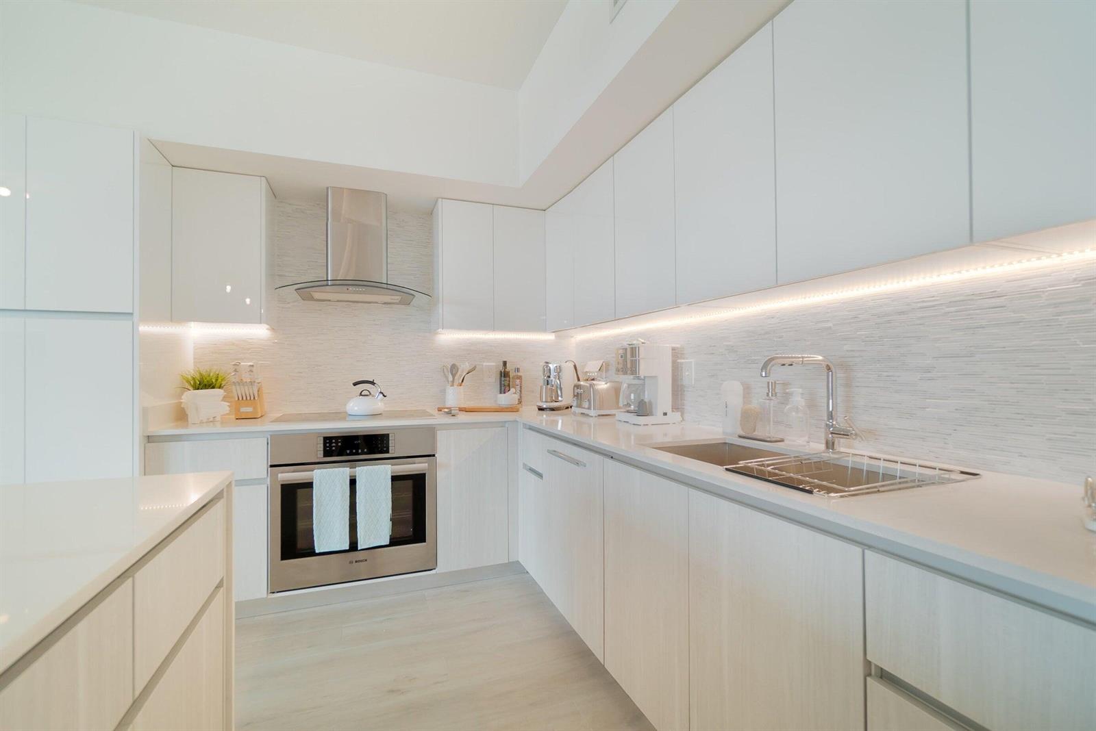 A modern kitchen features white cabinetry, stainless steel appliances, and light-colored countertops with under-cabinet lighting — 111 SE 1st Avenue # 514, Delray Beach FL 33444, DELRAY BEACH, FL