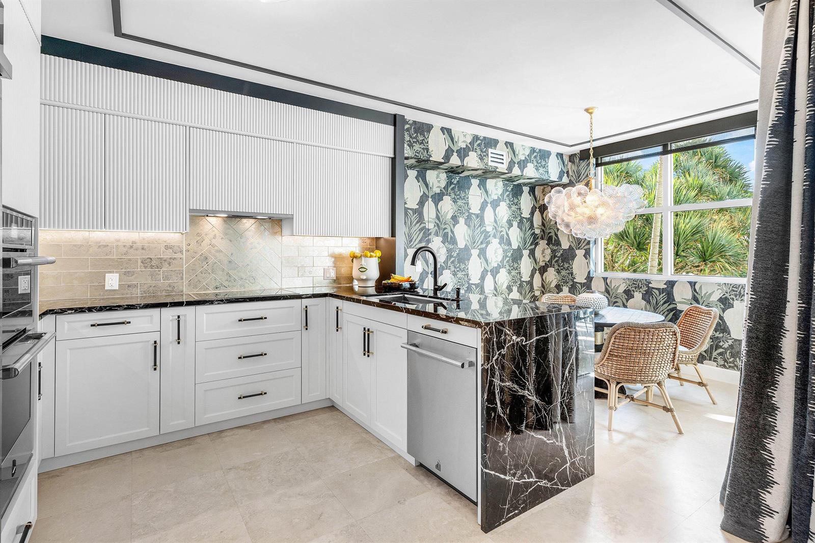 A kitchen with white cabinetry, black marble countertops, and patterned wallpaper in the dining area — 3700 S Ocean Boulevard # 202, Highland Beach FL 33487, HIGHLAND BEACH, FL