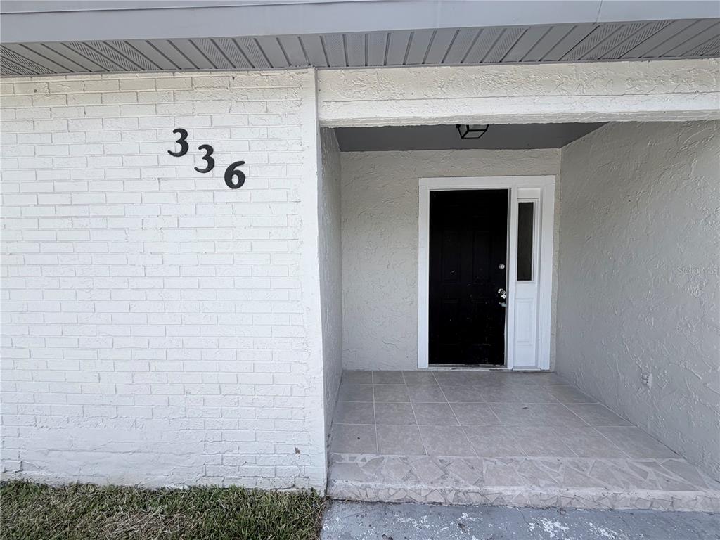 A white brick exterior wall with house number 336 leads to a covered tiled entryway — 336 MONTGOMERY COURT, KISSIMMEE, FL