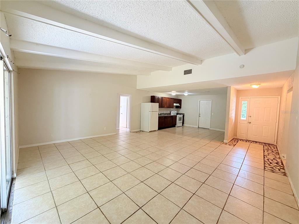 An open-concept living area features a tiled floor, vaulted beamed ceilings, and a kitchen corner — 336 MONTGOMERY COURT, KISSIMMEE, FL
