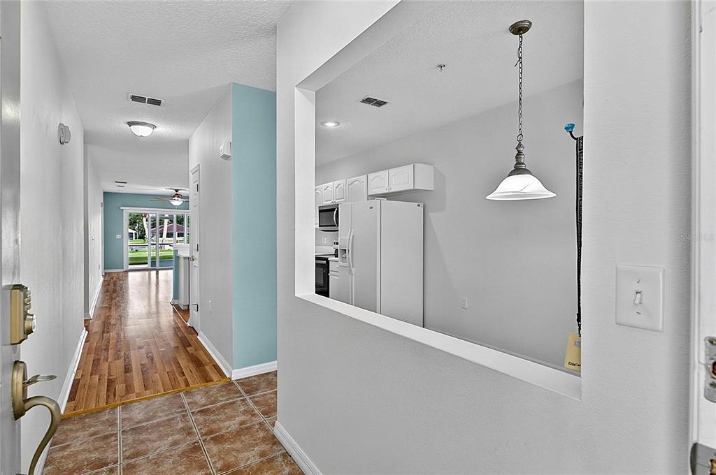An entryway with tile flooring leads to a hallway and a kitchen viewed through a cutout — 700 CANOPY WALK LANE UNIT 713, PALM COAST, FL