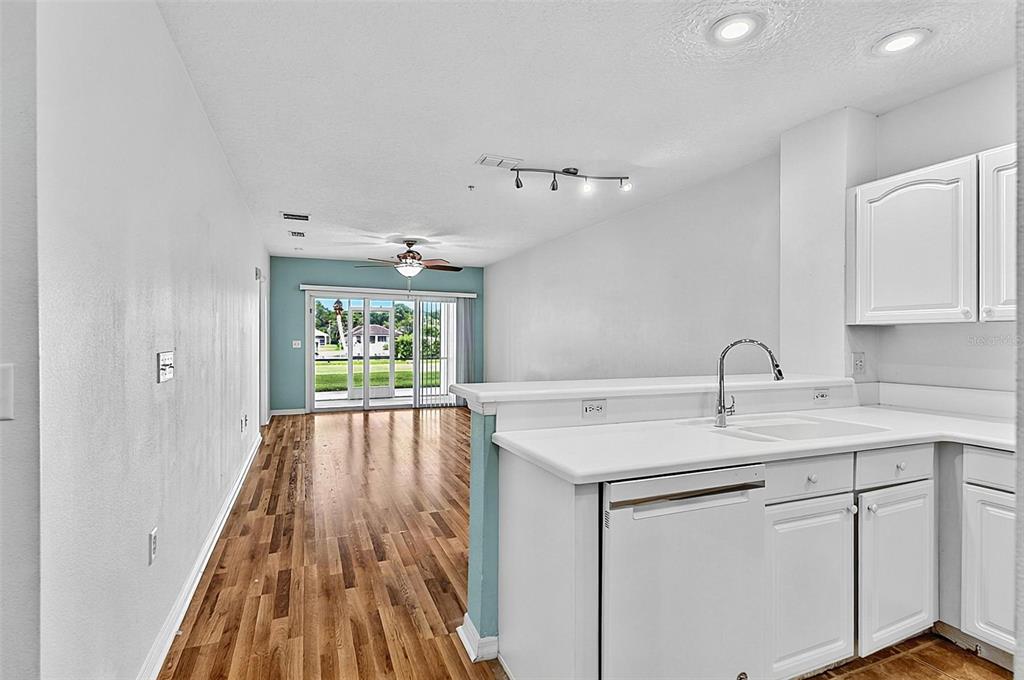 A kitchen with white cabinets overlooks a living area with wood floors and sliding glass doors — 700 CANOPY WALK LANE UNIT 713, PALM COAST, FL