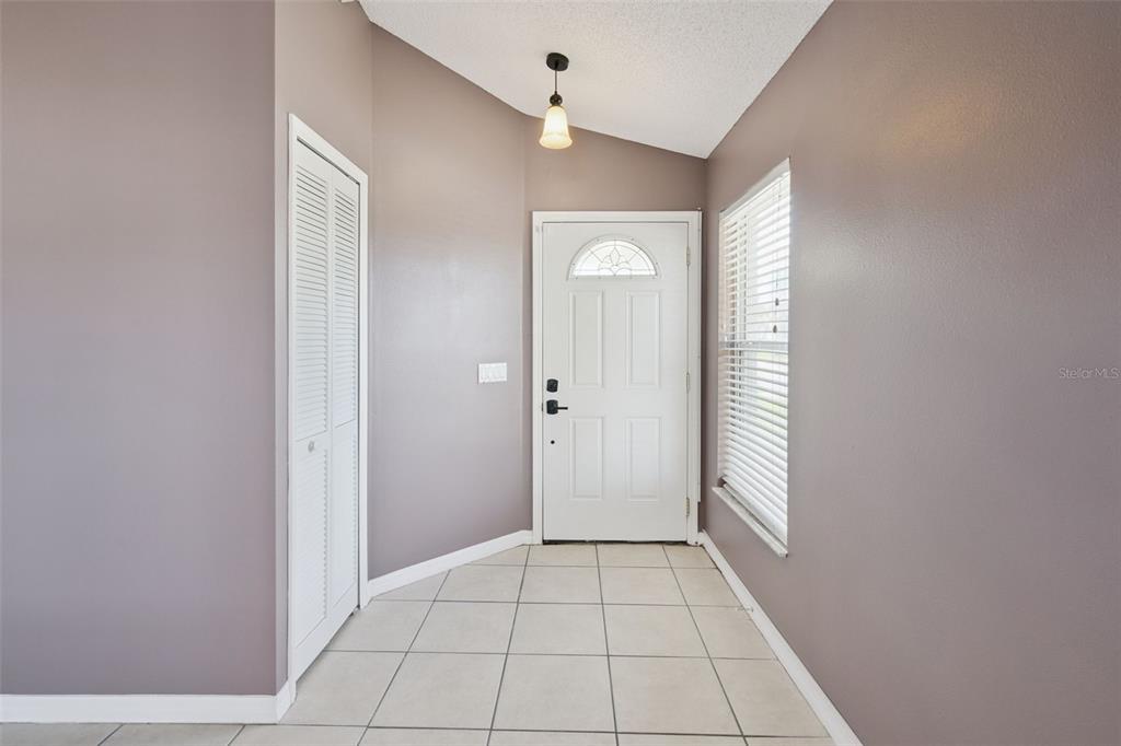 An entryway features light-colored floor tiles, mauve walls, a white front door, and a closet — 948 RIVECON AVENUE, ORLANDO, FL
