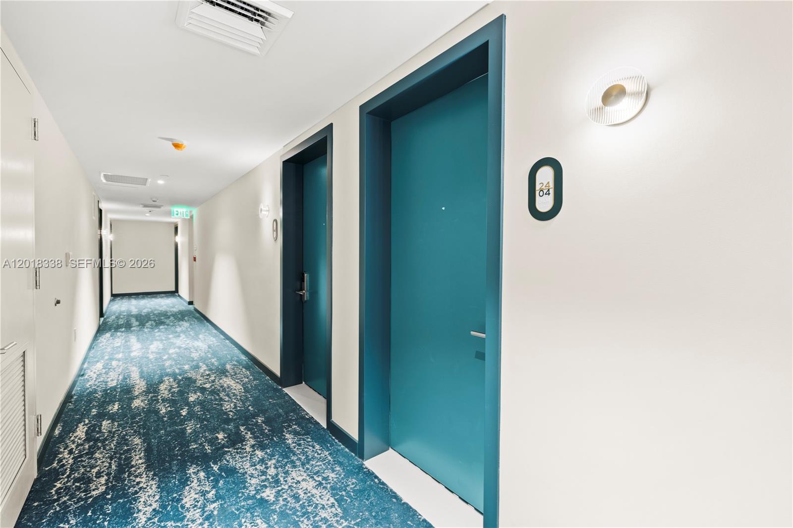 A hallway features teal doors, patterned blue carpeting, and white walls with modern light fixtures — 77 SE 5TH # 2404, Miami FL 33131, MIAMI, FL
