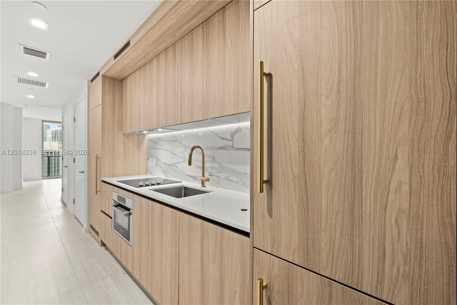 A modern kitchen features light wood cabinetry, a marble backsplash, and gold-toned hardware — 77 SE 5TH # 2404, Miami FL 33131, MIAMI, FL