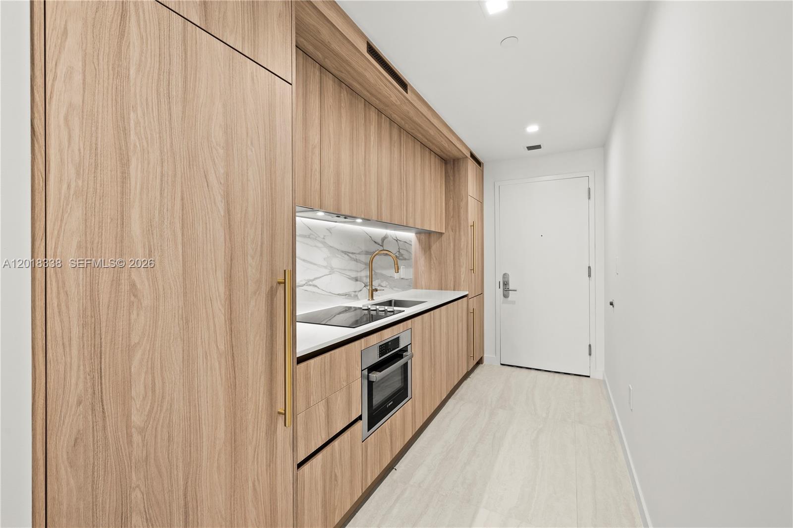 A modern galley kitchen features light wood cabinetry, white marble backsplash, and gold hardware — 77 SE 5TH # 2404, Miami FL 33131, MIAMI, FL