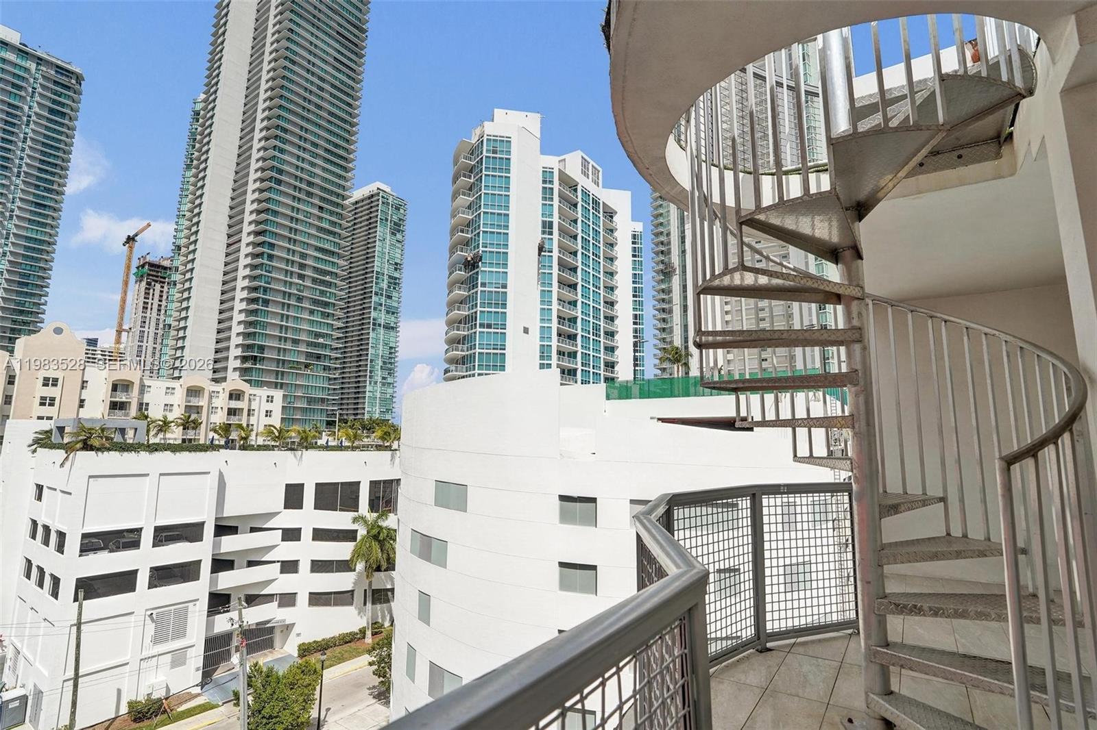 A balcony features a metal spiral staircase overlooking a city skyline with tall residential buildings — 481 NE 29th St # 702, Miami FL 33137, MIAMI, FL